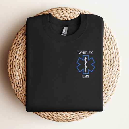 A black sweatshirt with a custom EMS embroidery design on the left chest area, featuring the outline of a star of life.