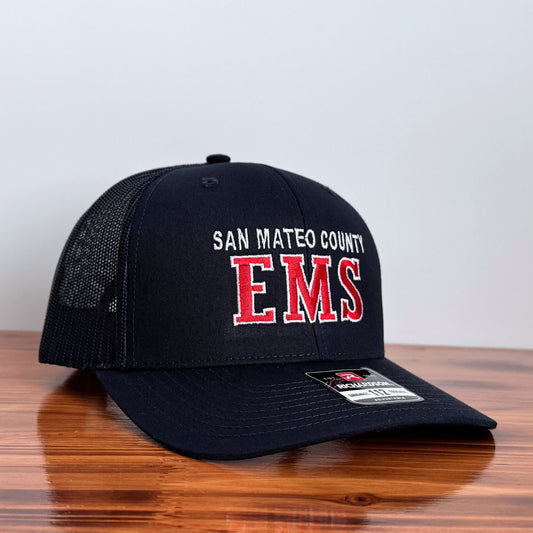 Black cap with 'San Mateo County EMS' text on a wooden surface