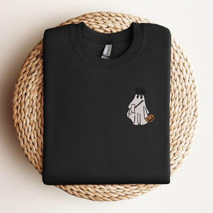 Black sweatshirt with an embroidered design of a ghost wearing a police officer's hat and holding a pumpkin candy bucket, displayed on a woven mat.